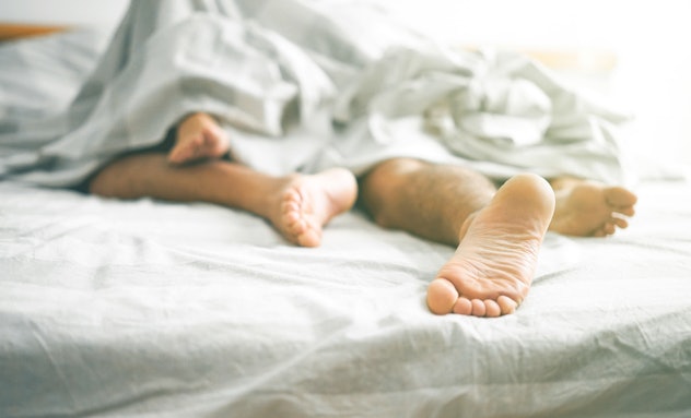 Couple in bed underneath the sheets, feet entangled 