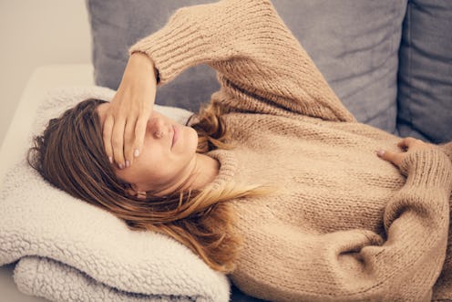 A depressed woman lying on her couch in a beige sweater putting her hand over her eyes