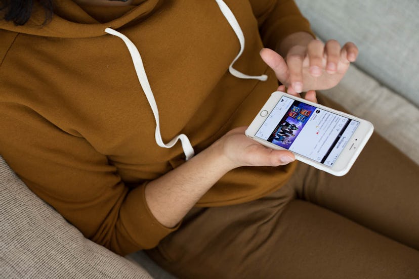 A depressed woman in a brown hoodie sitting on her couch and browsing her phone