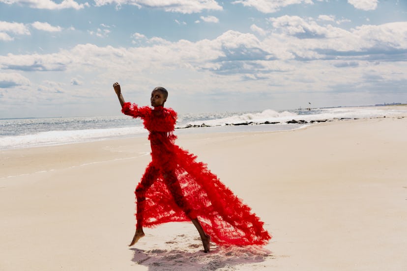 A model walking in a red Valentino dress with tulle and frills on a beach