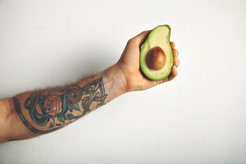A tattooed hand of a man holding an avocado.