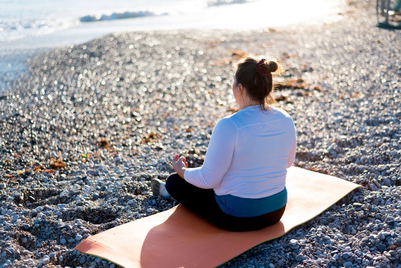 A woman sitting on a yoga mat, on the beach, meditating. 