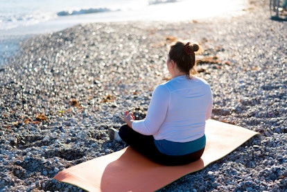 A woman sitting on a yoga mat, on the beach, meditating. 