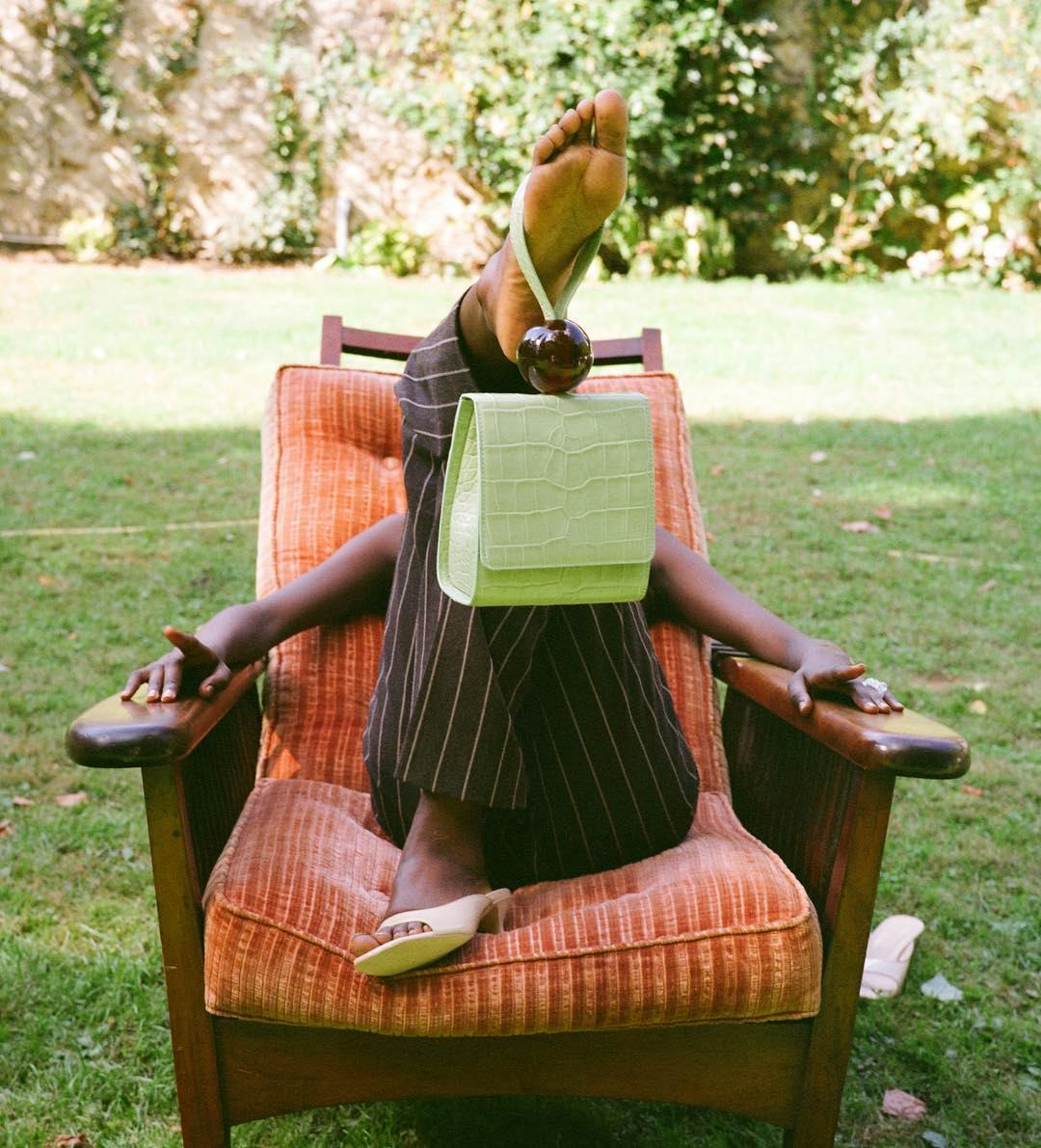 A model lying in a chair outside, while having a influencer approved bag dangling from her foot