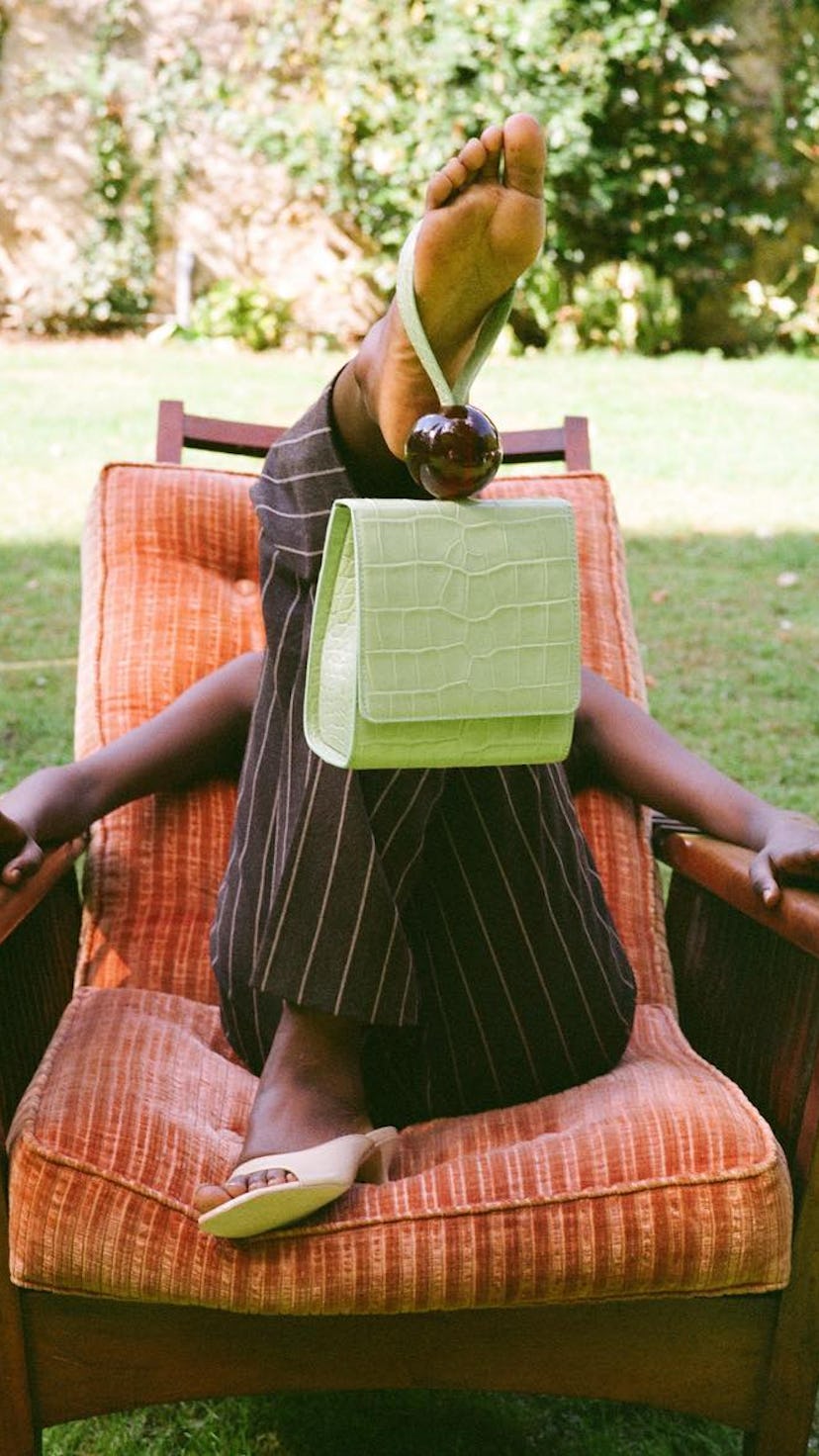 A model lying in a chair outside, while having a influencer approved bag dangling from her foot