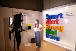 A woman filming in front of a camera with the words "Smart", "Alert" "Strong", "Kind" and "Brave" on...