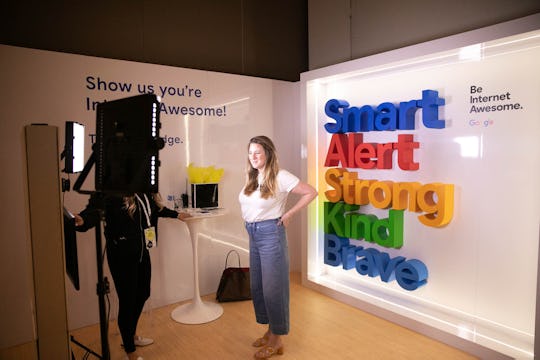 A woman filming in front of a camera with the words "Smart", "Alert" "Strong", "Kind" and "Brave" on...