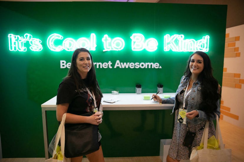 Two moms standing in front of a neon sign that says "it's cool to be kind" and "be internet awesome"