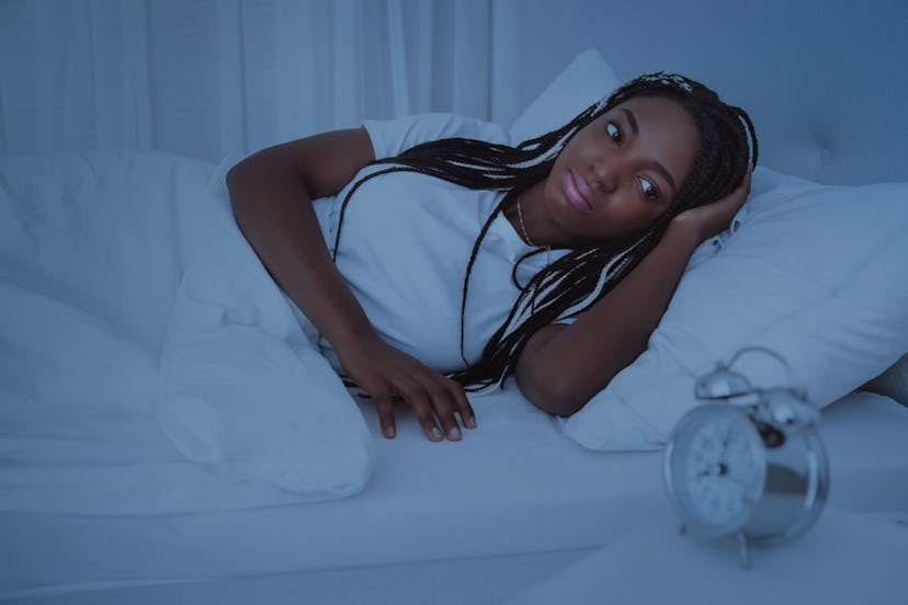 Lyme disease survivor lying in bed, anxiously looking at alarm clock.