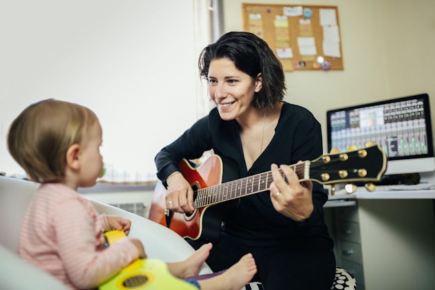 A mother playing a guitar and her toddler looking at her