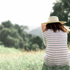 A woman sitting back turned to the camera on the grass in nature