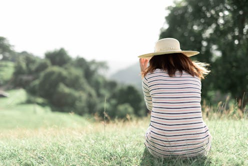 A woman sitting back turned to the camera on the grass in nature