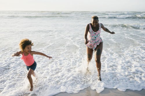 A mother and daughter playing and running around water on a beach