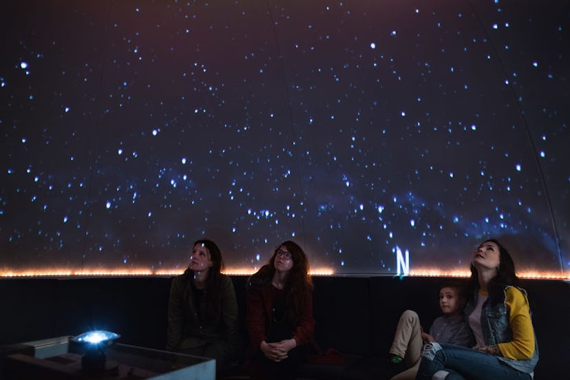 A mother and daughter next to two women watching an art installation of a night sky