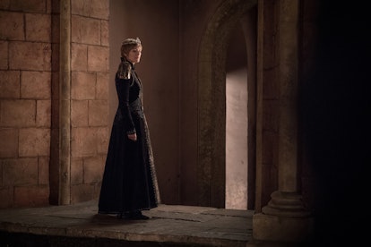 Cersei in Game of Thrones with short hair and a crown, and a long dress, standing in a corridor 
