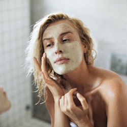 A young blonde lady putting an affordable skincare cream on her face