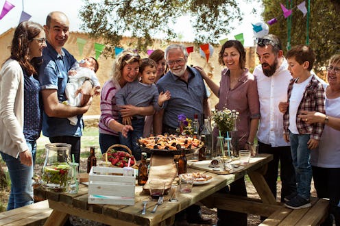 Three generations of a family, grandparents, parents and kids gathered over a lunch table outside