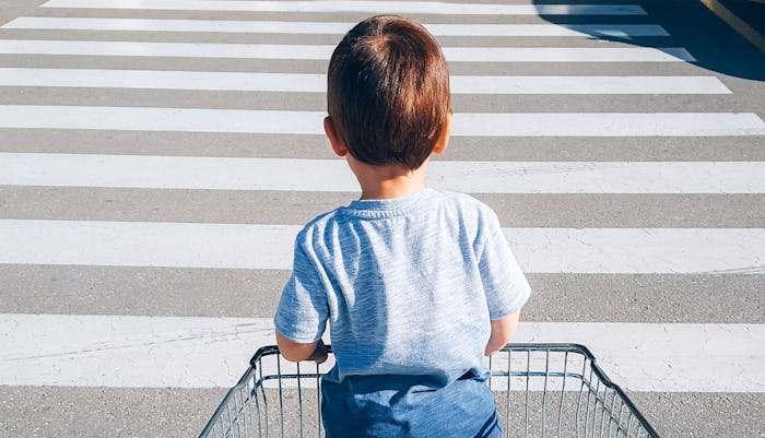 A kid standing in a shopping cart as he's being pushed over a pedestrian crossing