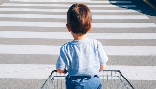 A kid standing in a shopping cart as he's being pushed over a pedestrian crossing