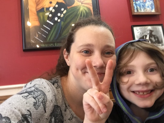 A mom and her 9-year-old kid cuddling and taking a photo with the kid showing a peace sign