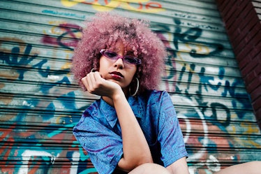 Young woman with pink hair in front of a graffitied background slaying the millennial game on social...