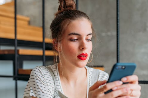 A young female with an updo and red lipstick holding her phone and turning off Autocorrect in iOS 10