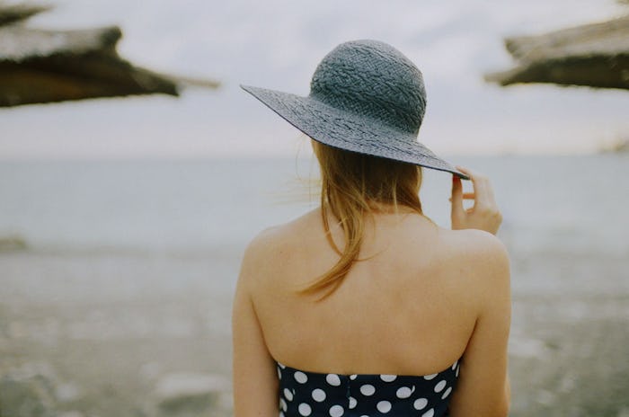 A woman with anxiety in a summer hat and a polkadot bathing suit stands in front of the sea on a clo...