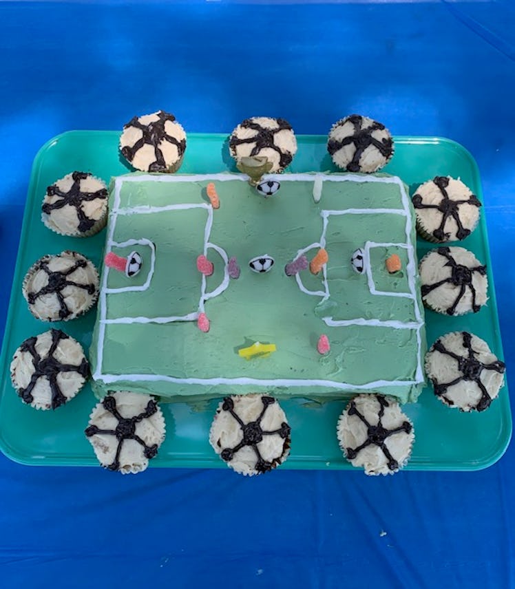 A birthday cake shaped like a soccer stadium surrounded by muffins