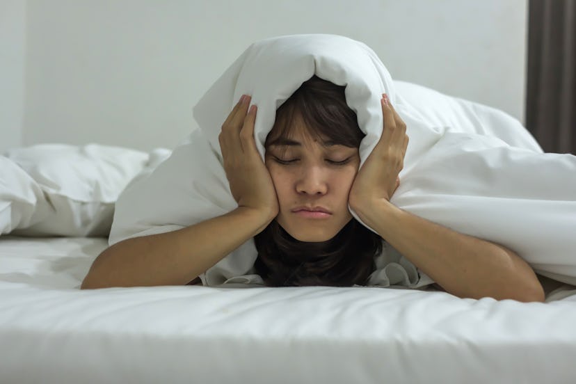 A woman holding a blanket over her head and ears as she experiences Insomnia as a result of anxiety