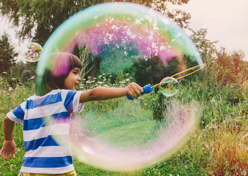 A little kid making a large soap bubble in a field 
