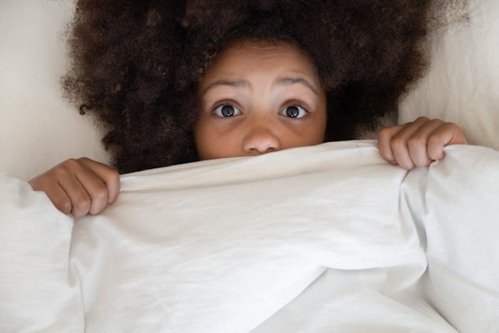 A girl lying in bed under a white blanket scared because of ghost stories