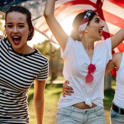 Three girls carrying the flag of the USA during a celebration of the Fourth of July