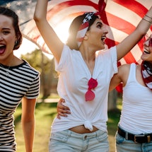 Three girls carrying the flag of the USA during a celebration of the Fourth of July