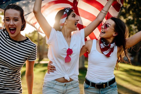 Three girls carrying the flag of the USA during a celebration of the Fourth of July