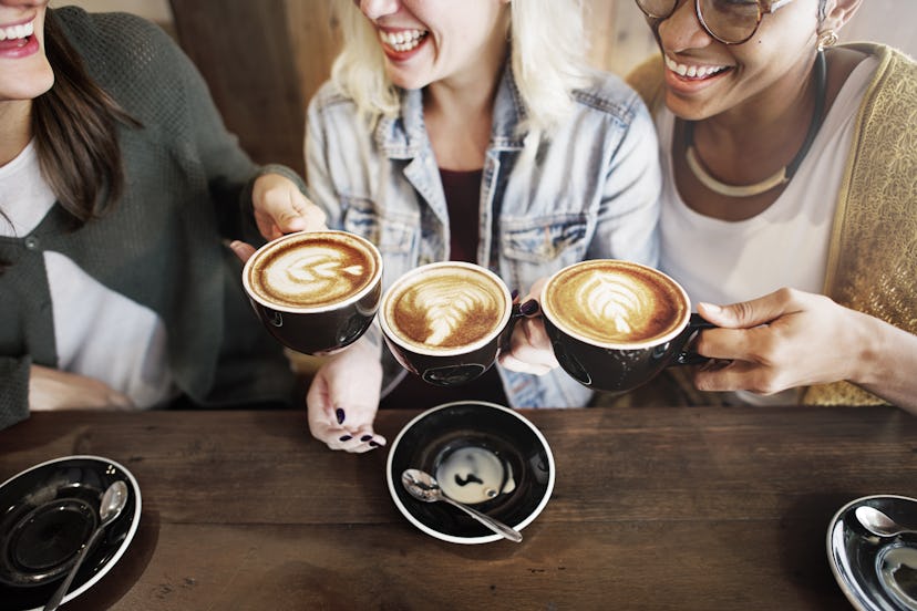 Three millennials sitting in a coffee shop holding their cups of coffee and showing the latte art th...