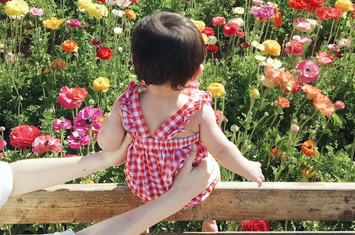A mom influencer holding her baby near flowers for a photo 
