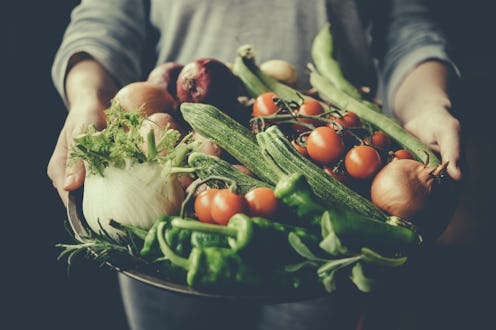 A person holding a plate with various vegetables including tomatoes, celery, bell peppers and cucumb...