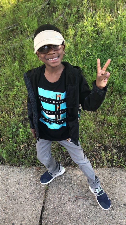 Latifah's son posing in a black-blue shirt, black hoodie, and grey denim jeans