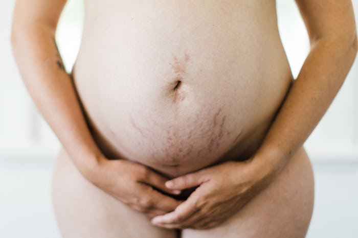 A nude pregnant surrogate holding on to her belly