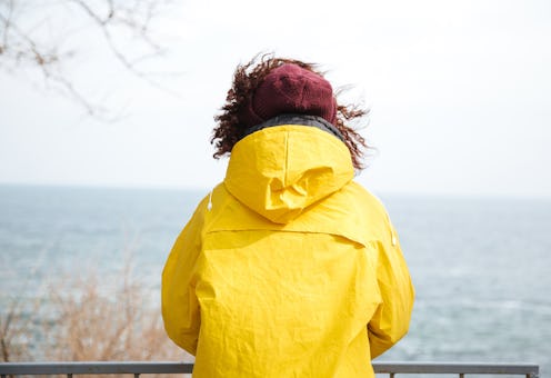 A woman in a yellow jacket looks out over a body of water. Here's how PTSD affects the brain, accord...