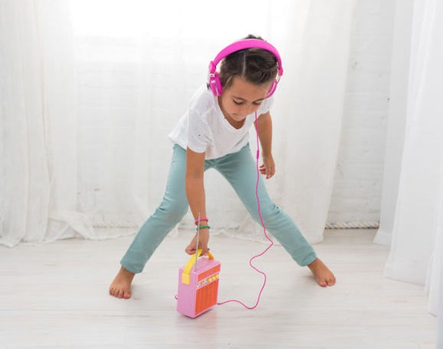 A little girl listening to music through pink headphones 
