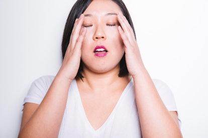 A brunette woman in a white shirt massaging her temples on her head