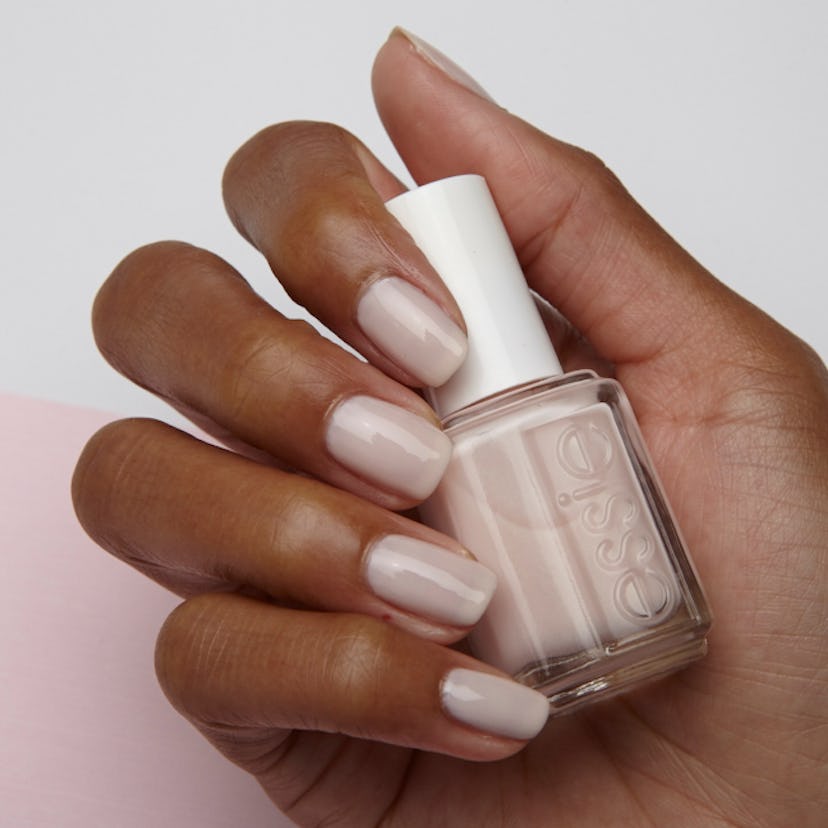 Female hand with Essie Ballet Slippers nail polish on, holding a bottle of the exact nail polish