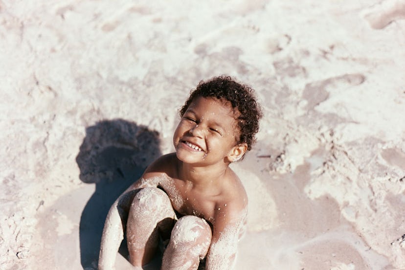 A little kid smiling while sitting in sand 