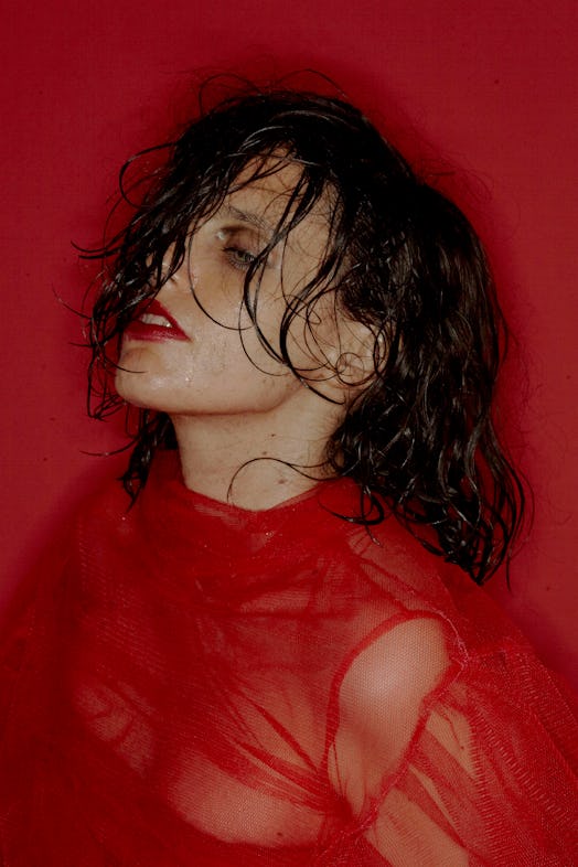 Anna Calvi with wet hair going over her face in a sheer red top in front of a red background