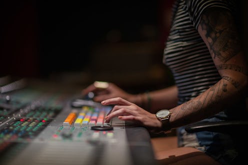 A woman in a striped shirt and tattoos on her arms is using a mixing board