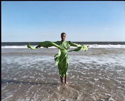 A model posing in a satin light-green Gucci dress on a beach