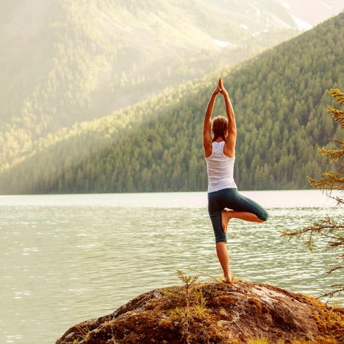 A woman doing yoga on a cliff with the view of a lake in the distance in Aspen