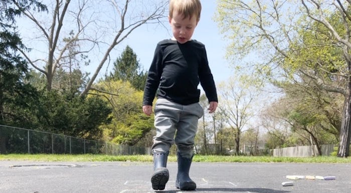 A 2-and-a-half-year-old boy walking in the street in rain boots