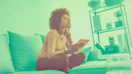 A woman sitting on a couch and holding a notebook thinking about how to pay off her debt